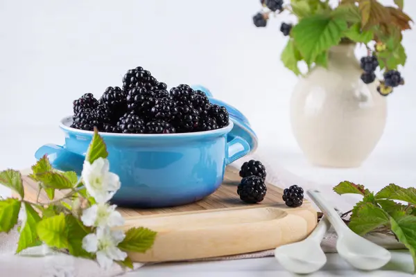 Ripe blackberries with leaves in a blue ceramic bowl on white table — Stock Photo, Image