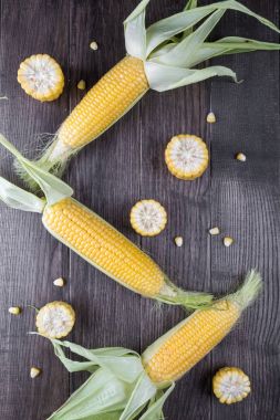 Ham mısır mısır koçanı ve koyu ahşap zemin üzerine yeşil yaprakları. Düz yatıyordu.