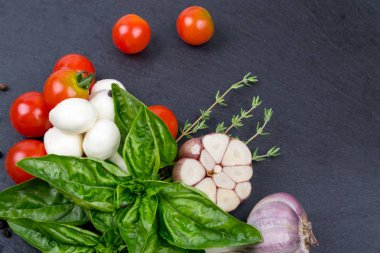 Mozzarella peyniri, domates ve taze fesleğen, limon, sarımsak. Salata için malzemeler. Kara kayrak taş üzerine. Üstten Görünüm.