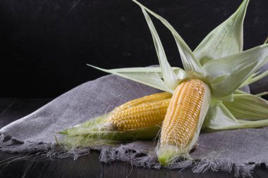 Olgun ham Mısır ve koyu ahşap zemin üzerine yeşil yaprakları. 