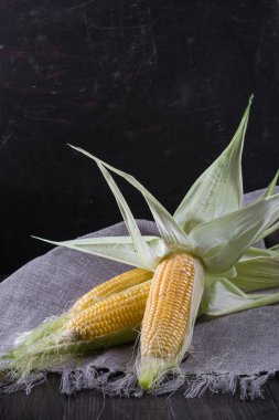 Olgun ham Mısır ve koyu ahşap zemin üzerine yeşil yaprakları. 