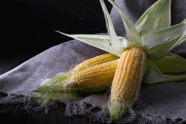 Olgun ham Mısır ve koyu ahşap zemin üzerine yeşil yaprakları. 