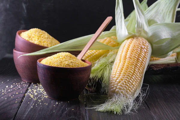 Corn grits polenta in a  ceramic bowl on white table with ripe  corn cob and green leaves