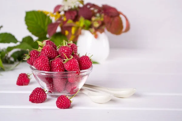 Red fresh raspberries in a glass bowl with green leaves — Stock Photo, Image