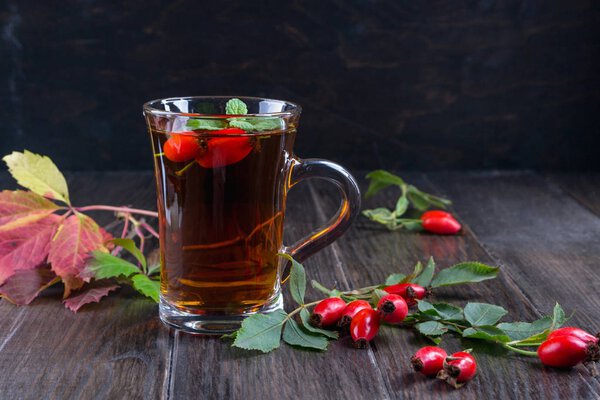 Healthy autumn  tea with dog roses, branch with berries on dark  background.