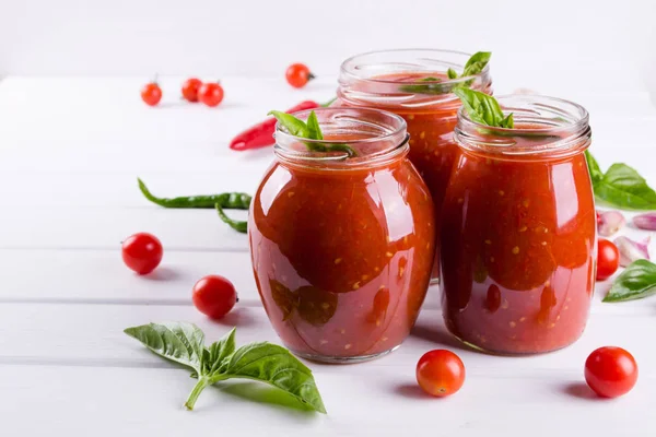 Molho de ketchup de tomate com tomate cereja e pimentão quente vermelho, alho e ervas em um frasco de vidro no fundo branco — Fotografia de Stock
