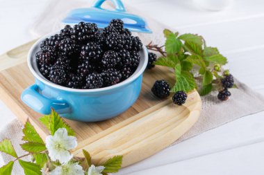 Beyaz masa üzerinde mavi bir seramik kase yapraklarla olgun böğürtlen