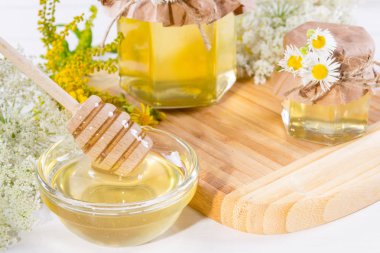 Tam taze sıvı bal tencere ve bal yaz kır çiçekleri beyaz masa üzerinde sopa