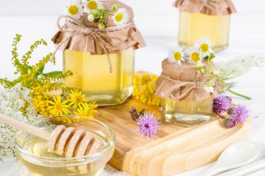 Tam taze sıvı bal tencere ve bal yaz kır çiçekleri beyaz masa üzerinde sopa