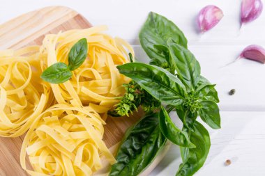 Pişmemiş makarna ve beyaz zemin üzerine sarımsaklı taze yeşil fesleğen. Düz yatıyordu.
