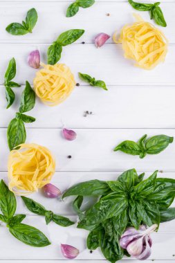 Sarımsak ve beyaz arka plan üzerinde ham makarna ile taze yeşil fesleğen. Düz yatıyordu.