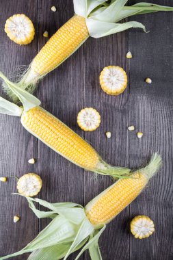 Olgun ham mısır mısır koçanı ve koyu ahşap zemin üzerine yeşil yaprakları. Düz yatıyordu.