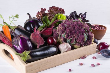 Taze çiğ mor homegrown sebze koyu ahşap masa üzerinde ürün yelpazesine. Karnabahar, patlıcan, pancar, havuç, patates, Erik, fesleğen, soğan, sarımsak, fasulye, marul. 