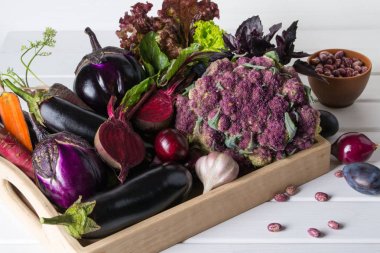 Taze çiğ mor homegrown sebze koyu ahşap masa üzerinde ürün yelpazesine. Karnabahar, patlıcan, pancar, havuç, patates, Erik, fesleğen, soğan, sarımsak, fasulye, marul. 