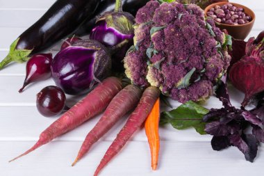 Taze çiğ mor homegrown sebze koyu ahşap masa üzerinde ürün yelpazesine. Karnabahar, patlıcan, pancar, havuç, patates, Erik, fesleğen, soğan, sarımsak, fasulye, marul. 