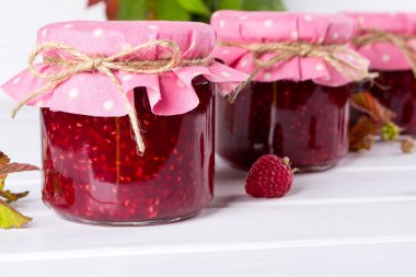 Satırlar ve Beyaz ahşap masa üzerinde taze ahududu Frambuaz reçeli ile kavanoz yerleştirilir