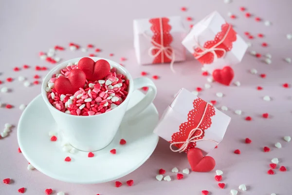 Festive background.  Coffee cup, full of multicolor sweet sprinkles sugar candy hearts and packing Valentine\'s  Day gifts.  Love and Valentine\'s day concept.