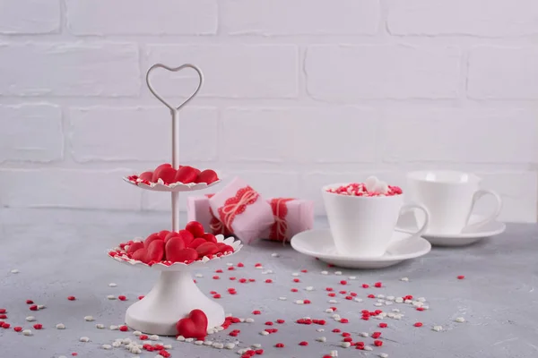 Festive background.  Coffee cup, white two tier serving tray full of multicolor sweet sprinkles sugar candy hearts and packing Valentine's  Day gifts  Love and Valentine's day concept.