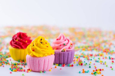Üç minyatür çok renkli şeker cupcakes sprinkles ile ışık arka plan üzerinde