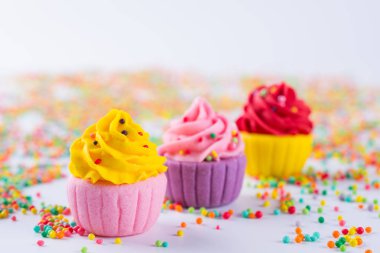 Üç minyatür çok renkli şeker cupcakes sprinkles ile ışık arka plan üzerinde