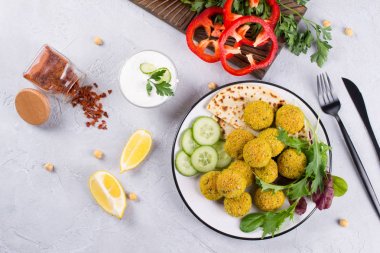 Ev yapımı baharatlı nohut falafel hafif beton arka plan üzerinde taze sebze ve bir tabak yoğurt ile süslenmiş. İsrail mutfağı kavramı