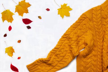 Autumn composition.Warm yellow knitted sweater, leaves on white background. Flat lay, top view, copy space