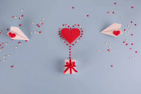 Love concept - Valentines day, anniversary or wedding celebration concept. Flat lay. Top view. Copy space. Origami paper heart balloon with gift box flying. On pastel blue background.