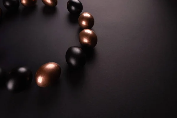 Golden and black eggs, laid out in a circle on black background. Flat lay, Top view, copy space.