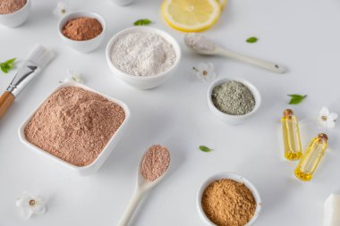 Kırmızı kil tozlu seramik kase, ev yapımı yüz ve vücut maskesi için malzemeler ya da fırça ve beyaz arka planda çiçek açan kiraz filizleri. Spa ve vücut bakımı kavramı.