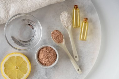 Kırmızı kil tozlu seramik kase, ev yapımı yüz ve vücut maskesi için malzemeler ya da fırça ve beyaz arka planda çiçek açan kiraz filizleri. Spa ve vücut bakımı kavramı.