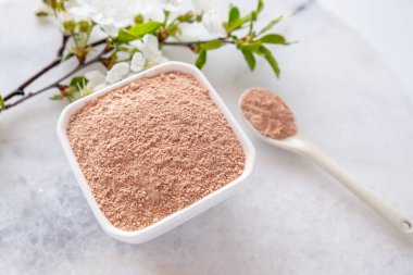 Kırmızı kil tozlu seramik kase, ev yapımı yüz ve vücut maskesi veya fırça ve beyaz arka planda çiçek açan kiraz filizleri için. Spa ve vücut bakımı kavramı.