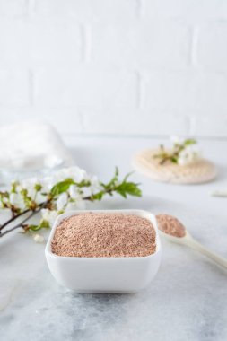 Kırmızı kil tozlu seramik kase, ev yapımı yüz ve vücut maskesi için malzemeler ya da fırça ve beyaz arka planda çiçek açan kiraz filizleri. Spa ve vücut bakımı kavramı.