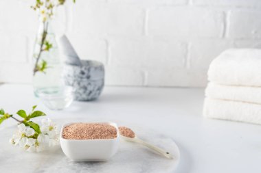 Kırmızı kil tozlu seramik kase, ev yapımı yüz ve vücut maskesi için malzemeler ya da fırça ve beyaz arka planda çiçek açan kiraz filizleri. Spa ve vücut bakımı kavramı.