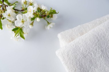 Beyaz arka planda çicek açan beyaz kirazlı tüylü banyo havluları. Spa ve vücut bakımı konsepti. Spa kompozisyonu. Boşluğu kopyala