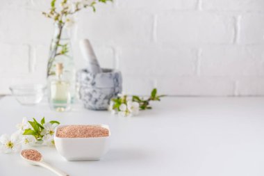 Kırmızı kil tozlu seramik kase, ev yapımı yüz ve vücut maskesi için malzemeler ya da fırça ve beyaz arka planda çiçek açan kiraz filizleri. Spa ve vücut bakımı kavramı.