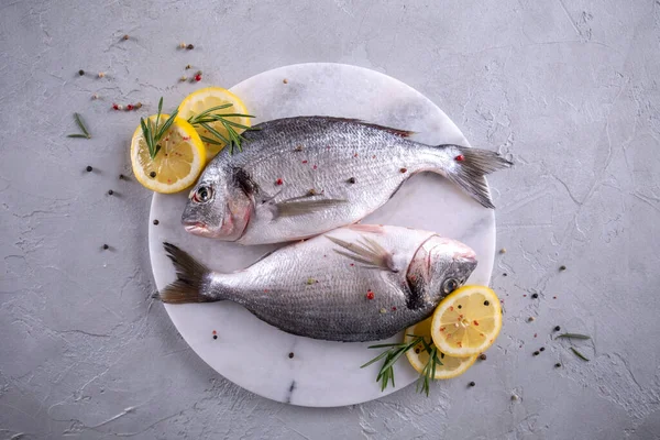 Fresh raw sea bream fish decorated with lemon slices, herbs on gray background. Healthy food concept, top view, copy space