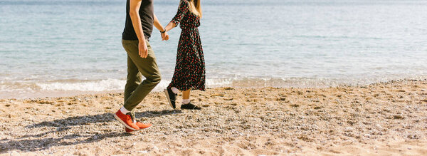 парень и девушка идут по солнечному пляжу держа за руку
