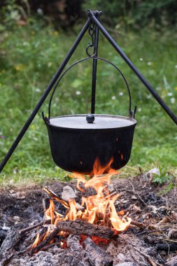 Tencereye ile kamp ateşi yukarıda tripod üzerinde asılı kapak