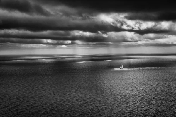 Sea scape with cloudy atmosphere and sailing boat and sun rays — Stock Photo, Image