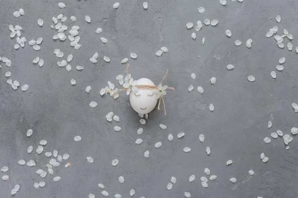 Huevo Blanco Con Cara Sobre Fondo Gris Con Pétalos —  Fotos de Stock