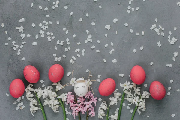 White egg with face with pink eggs in row with blooming hyacinths