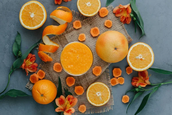 Top view of orange smoothie decorated with alstroemeria, halfs of orange and carrot rounds