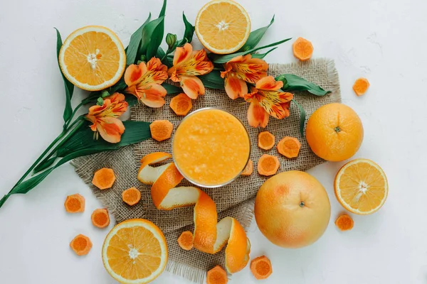 Top view of orange smoothie decorated with alstroemeria, halfs of orange and carrot rounds