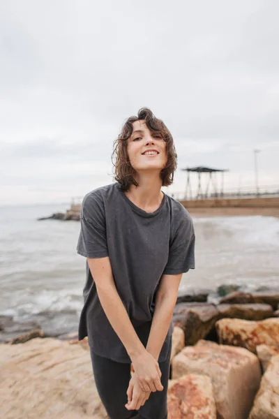 바다 근처 돌 위에 서서 미소를 짓는 여자 — 스톡 사진