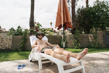 Güneş banyosu yapan bir adam havuz kenarında güneşleniyor.