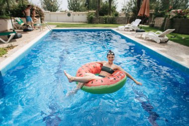 Güzel genç bir kadın yüzme havuzunda şişme yüzükte dinleniyor.