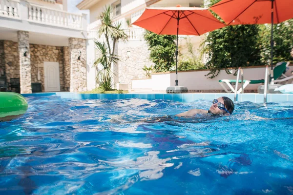 man swims in pool near villa