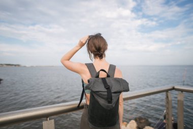 Sırt çantalı kız deniz kenarında geziyor.