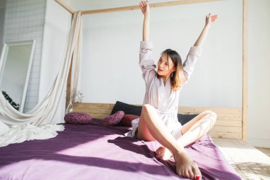 Güzel genç bir kadın gülümsüyor ve yatakta eğleniyor.