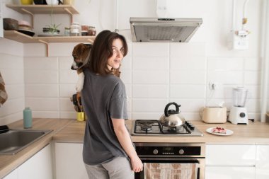 Genç bir kadın mutfakta köpekle yemek pişiriyor.